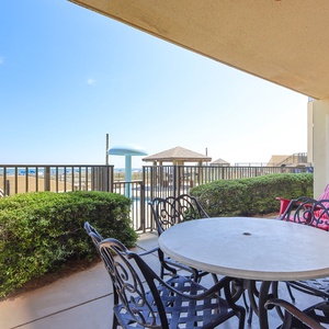 A round table with black metal chairs overlooks a pool area and lush greenery, inviting relaxation on the ground floor patio