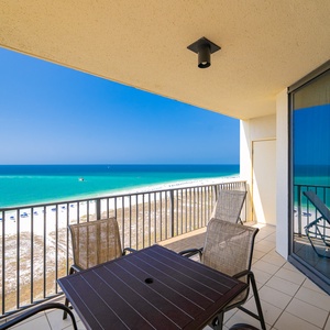 Expansive view of the beach with white sand and gentle waves, framed by lush greenery and a boardwalk leading to the shore