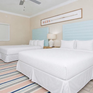 Guests will sleep peacefully in this inviting room with two queen beds, soft decor, and a cozy vibe