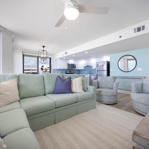 Living area features a light green sectional sofa with decorative pillows, two accent chairs, and an open view to the kitchen
