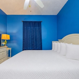 This bedroom features a large white bed, a TV for entertainment, and vibrant blue walls for a refreshing atmosphere