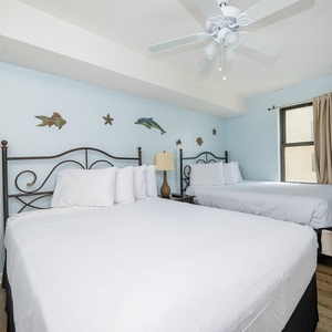 This guest bedroom features two queen beds with white linens, light blue walls, and decorative fish accents