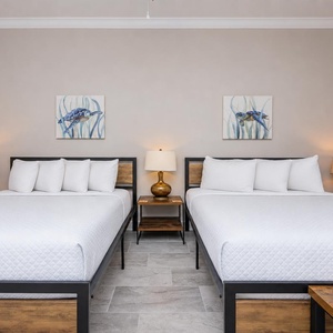 Dual queen guest room with soft lighting, fluffy pillows, and soothing coastal vibe