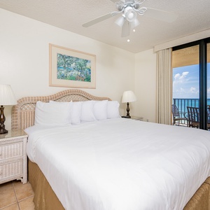 Spacious master bedroom with a king bed, coastal decor, and sliding glass doors leading to beautiful views