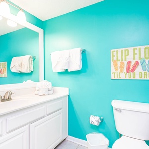 White vanity, vibrant turquoise walls, and fresh towels in this cheerful bathroom, featuring a playful flip-flop sign