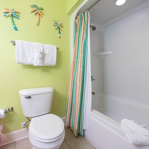 Guest bathroom featuring vibrant green walls, plush towels, and a colorful striped shower curtain