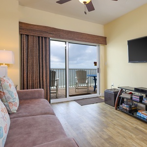 This cozy living area features a plush sofa, a TV, and a stunning beachfront view from the blacony door