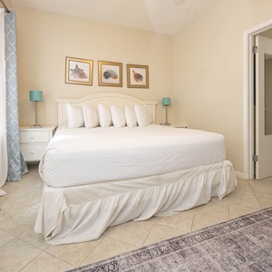 Bright guest room featuring a king bed with white linens, decorative artwork, and soft blue curtains, creating a serene vibe