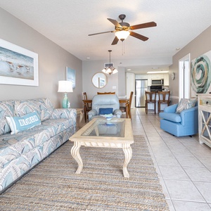Coastal living area features a patterned sofa with queen sleeper, glass coffee table, and a view into the dining area