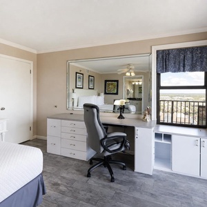 Well-lit master bedroom featuring a comfortable king bed, a stylish workspace with a chair, and a scenic view from the window