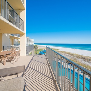 The extended balcony features a dining table and lounge chairs, offering a serene view of the beach and turquoise waters