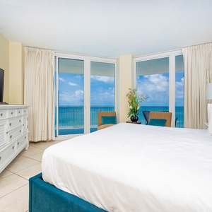 The master bedroom features a plush bed, a large TV, and stunning beachfront views through expansive windows