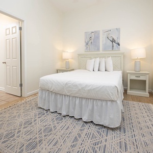 Bright guest bedroom featuring a plush queen bed, soft lighting, and coastal artwork, creating a serene retreat