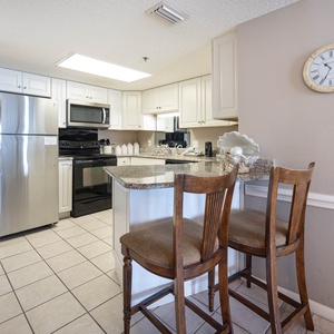 Bright, fully-equipped kitchen features granite countertops, sleek appliances, and a breakfast bar with two wooden stools