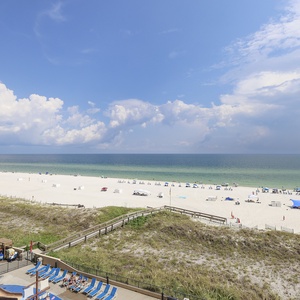 The view showcases a pristine beach with white sand, sun loungers, and a sparkling pool area, inviting relaxation and fun