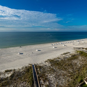 A serene beachfront view showcases white sand, gentle waves, and colorful umbrellas lining the shore under a clear blue sky