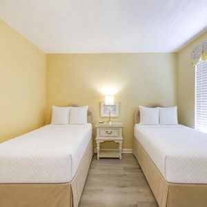 Guest bedroom featuring two twin beds, a bedside table with a lamp, and cheerful yellow walls