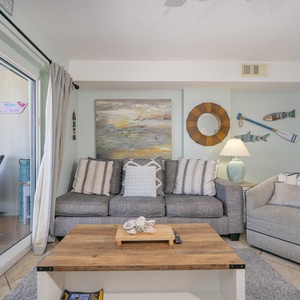 The living area features a sofa with decorative pillows, a warm lamp, and a view of the beach through large sliding doors