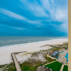 Coastal view from the balcony, showcasing sandy shores and gentle waves under a dramatic blue sky