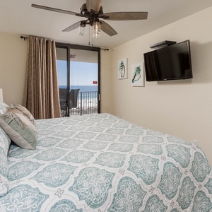 Cozy master bedroom featuring a king bed with beach decor and a balcony offering a beautiful view of the beach