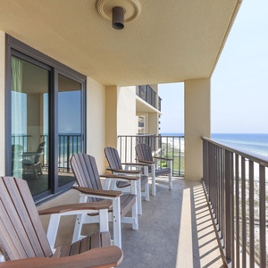 The balcony features four wooden chairs overlooking a serene beach front with soft, white sand and clear blue waters