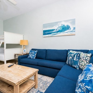 Living area features a blue sectional sofa with decorative pillows, a wooden coffee table, and a cozy twin bunk bed
