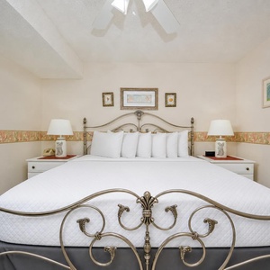 A stylish bedroom features a king bed with decorative pillows, charming lamps, and coastal artwork on the walls