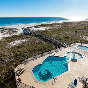 Expansive beach front view showcases a serene pool area with seating, leading to the inviting white sand beach
