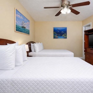 This guest bedroom features two comfortable beds, a TV, and vibrant ocean-themed artwork for a relaxing stay