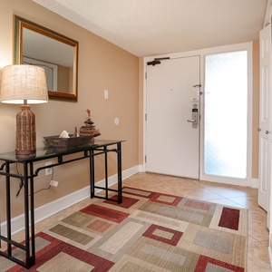 The entryway features a stylish console table with a lamp, decorative accents, and a colorful area rug against a neutral wall