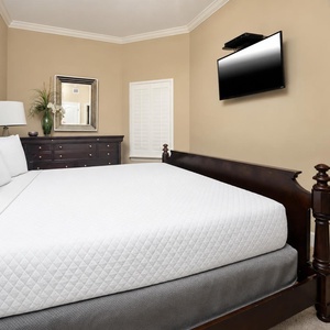 This cozy guest bedroom features a plush king bed, a mounted TV for entertainment, and elegant decor with warm tones