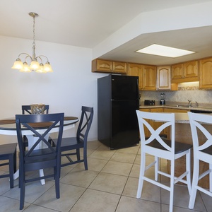 Kitchen featuring light wood cabinetry, a black refrigerator, and the dining area with a round table and blue chairs