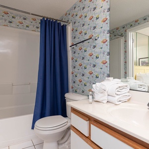 Refresh in the cheerful bathroom, featuring a tub-shower combo, bright floral wallpaper, and neatly arranged towels