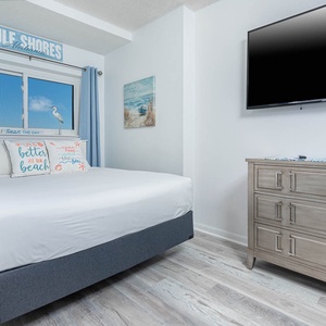 This cozy sleeping nook features a comfortable bed, a large TV, and a beach-themed decor with a lovely view of Gulf Shores