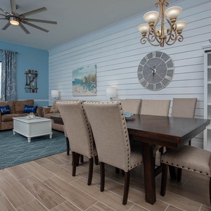 Bright blue walls complement the cozy living area with a plush sofa, dining table, and beach-themed decor for a relaxed vibe