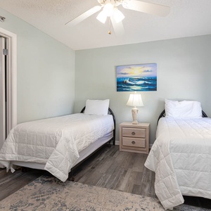 Guest bedroom featuring two twin beds, a bedside lamp, and a coastal painting, creating a serene atmosphere