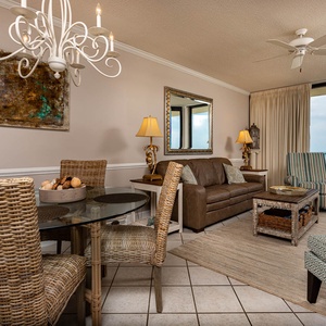 Cozy living area features a brown sofa, glass dining table, and stunning views of the beach