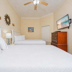 Soothing guest bedroom featuring two comfortable queen beds, a wall-mounted TV, and charming coastal decor