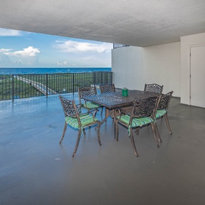 The extended balcony features a dining table with green striped chairs, offering a serene view of the beach and gulf waters