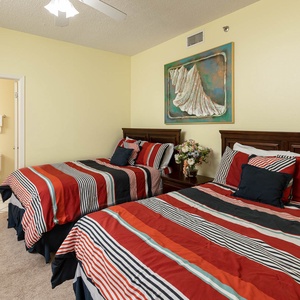 This bright guest bedroom features two queen beds, a decorative wall art piece, and an en-suite bathroom entrance