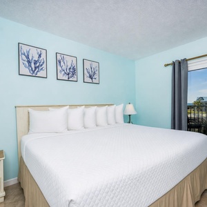 The master bedroom features a large bed with white linens, light blue walls, and a balcony view for a relaxing retreat