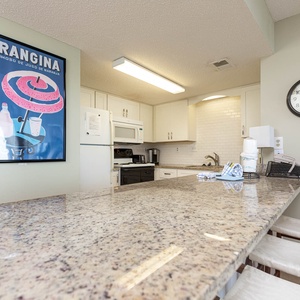 The kitchen features granite countertops, modern appliances, and a vibrant vintage poster, perfect for meal prep or gathering