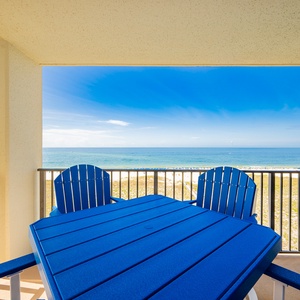 Bright blue chairs surround a table on the balcony, offering a serene view of the beach and gulf under a clear sky