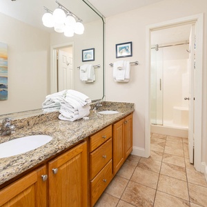 Spacious master bathroom with dual sinks, elegant granite countertops, and vibrant art that enhances your stay