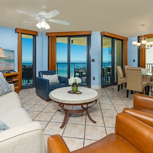 Living area features a light sofa, leather chairs, a coffee table, and a view of the beachfront through large windows