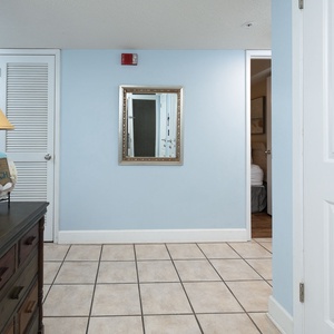 The entryway features a charming wooden dresser, a decorative lamp, and a large mirror against soft blue walls