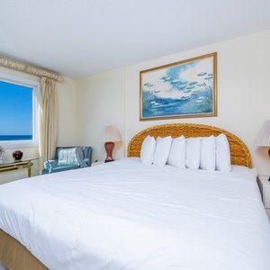 This bedroom features a large bed, elegant decor, and a stunning beachfront view through the expansive window