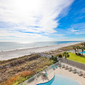 This inviting space features a stunning beachfront view, with a relaxing pool area below and vibrant blue skies above
