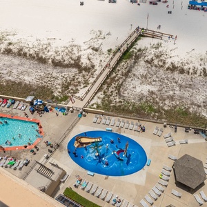 The vibrant pool area features a fun pirate ship splash park and loungers, with a scenic view of the beach beyond