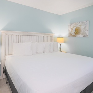 The master bedroom features a large bed with crisp white linens, soft blue walls, and warm lighting for a serene retreat